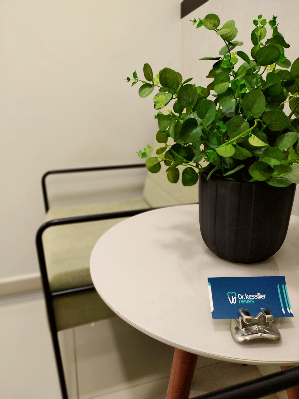 Mesa de apoio da recepção com cartão do Dr. Kessiller Neves e planta decorativa