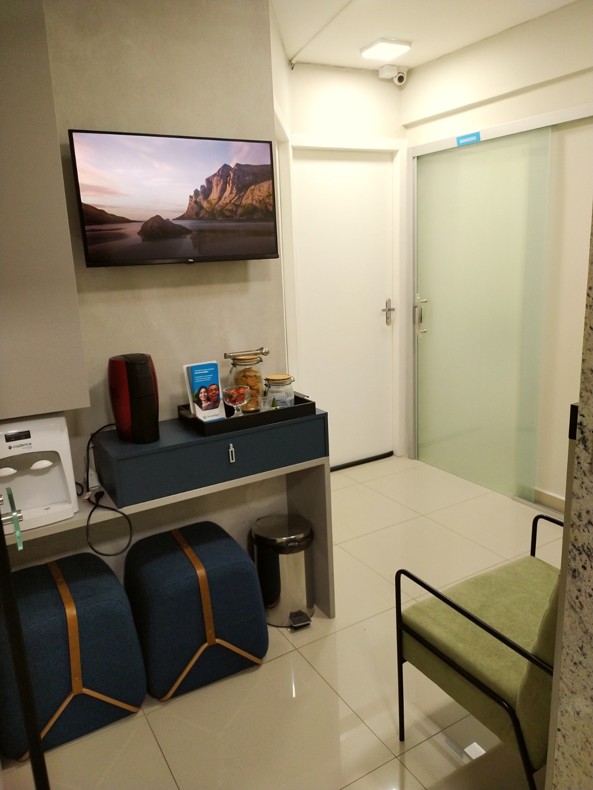 Recepção do consultório com TV, cafeteira, água e poltronas para os pacientes