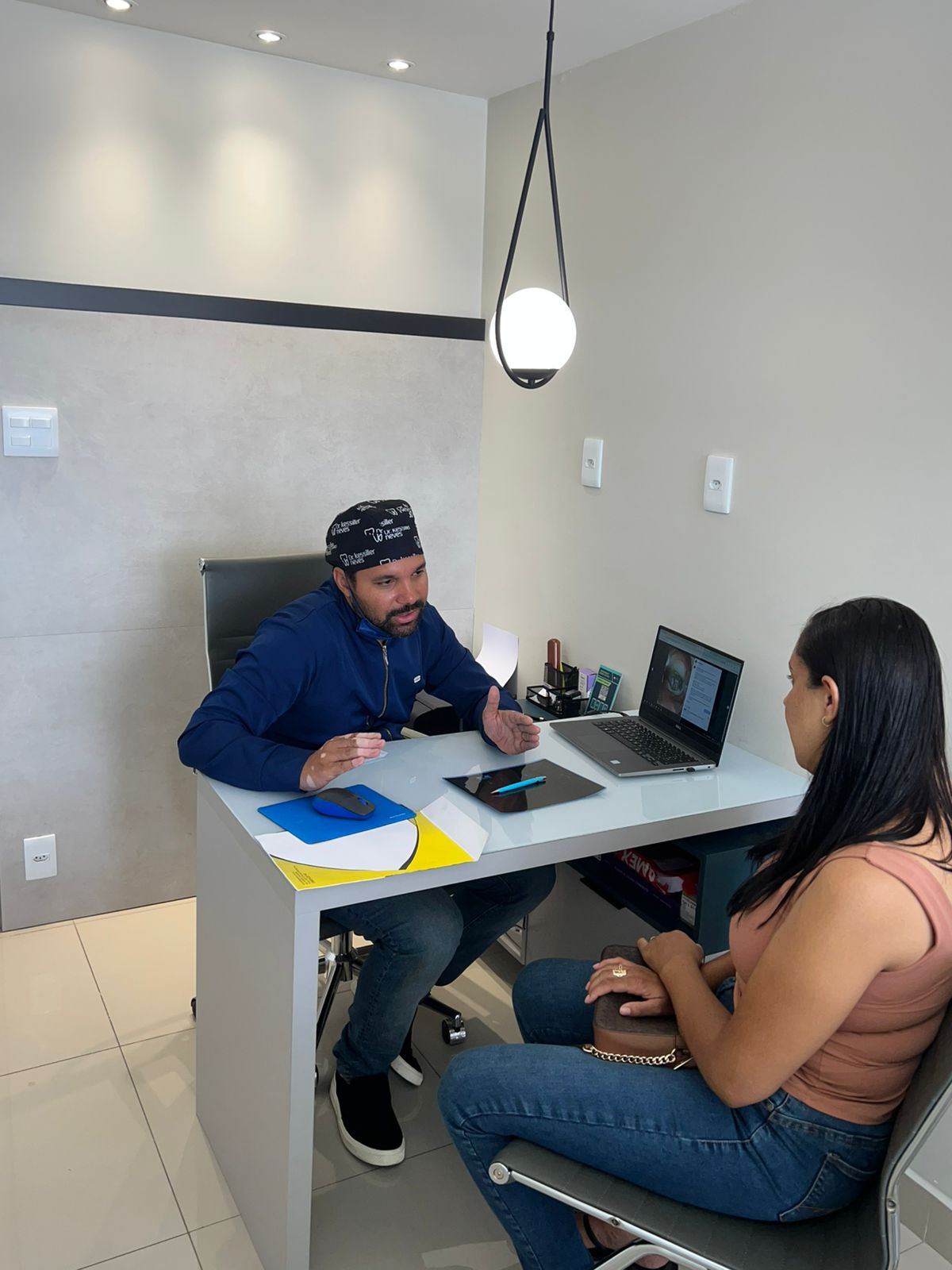 Dr. Kessiller Neves explicando o planejamento do tratamento para uma paciente na sala de consulta